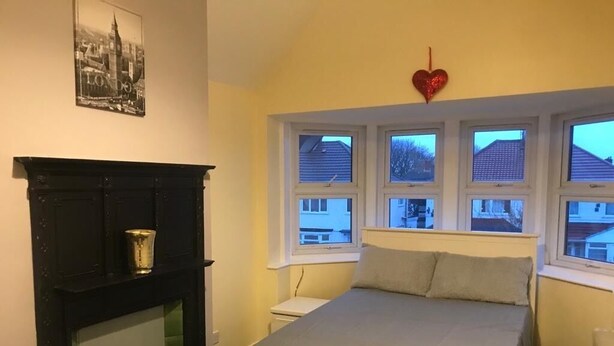 Un dormitorio con cama, mesita de noche, cómoda y ventana con vistas a casas.
