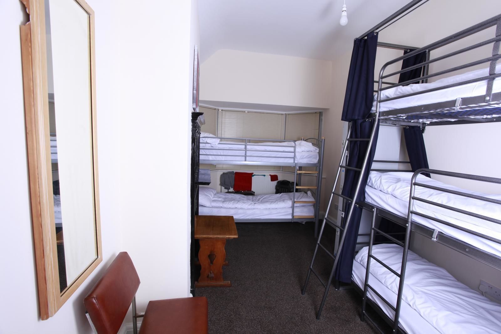Une chambre de dortoir avec des lits superposés, une chaise en bois, une petite table et un miroir au mur.