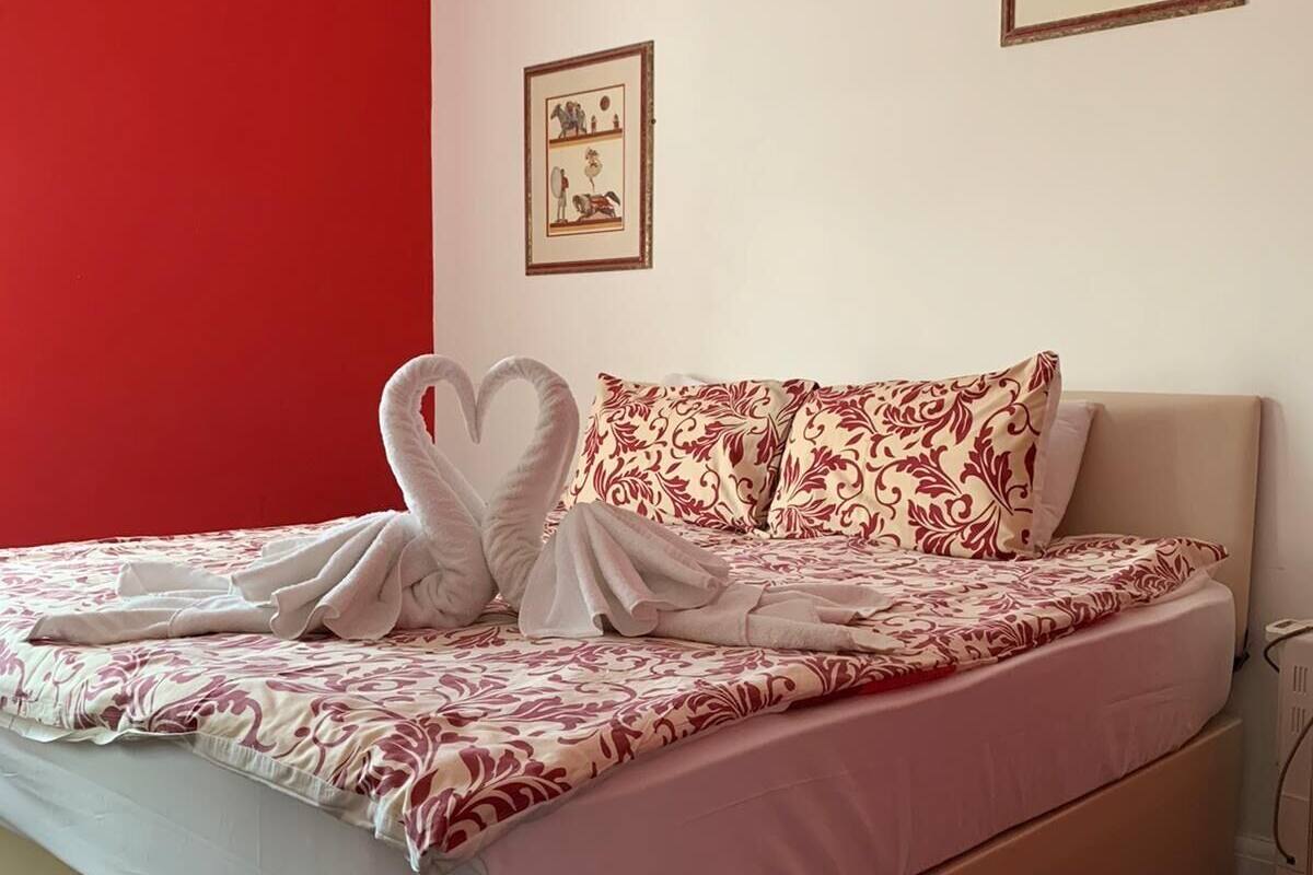 A neatly made bed with a heart-shaped towel arrangement, a patterned bedspread, and two framed pictures on the wall.