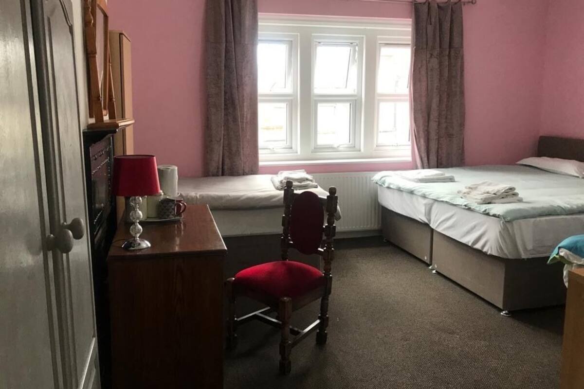A bedroom with a single bed, a desk with a lamp, a chair, and a window with curtains.