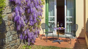 A two-story building with a stone wall, a balcony with green shutters, and a table with chairs outside. - Cà del Moro Resort (Pontremoli)