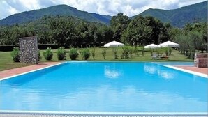 A swimming pool with a stone pillar, surrounded by a grassy area and white tents. - Cà del Moro Resort (Pontremoli)
