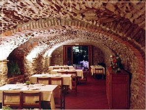 An indoor dining area with stone arches, tables set with white tablecloths, and chairs. - Cà del Moro Resort (Pontremoli)