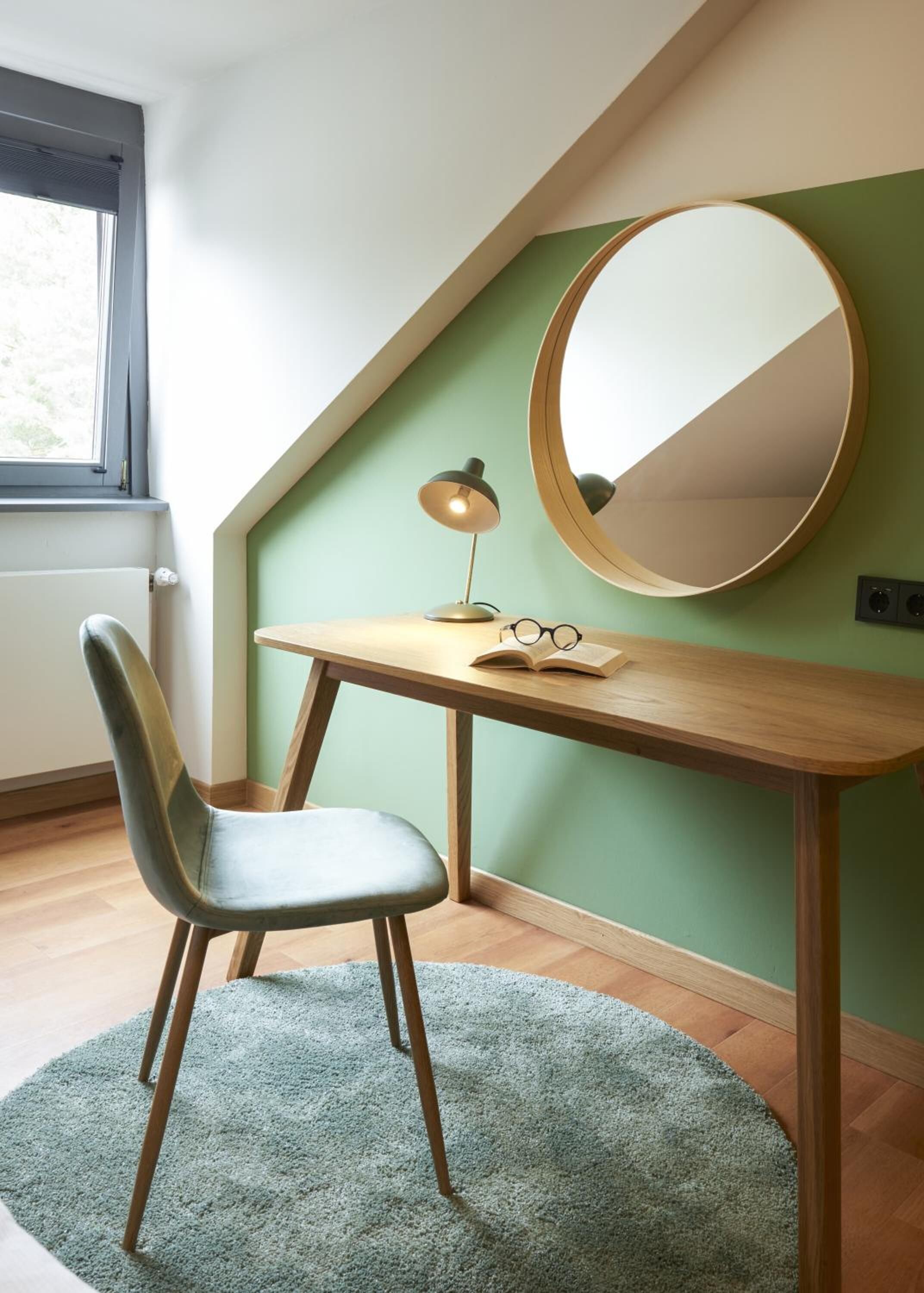 A study room with a desk, chair, round mirror, and a lamp.