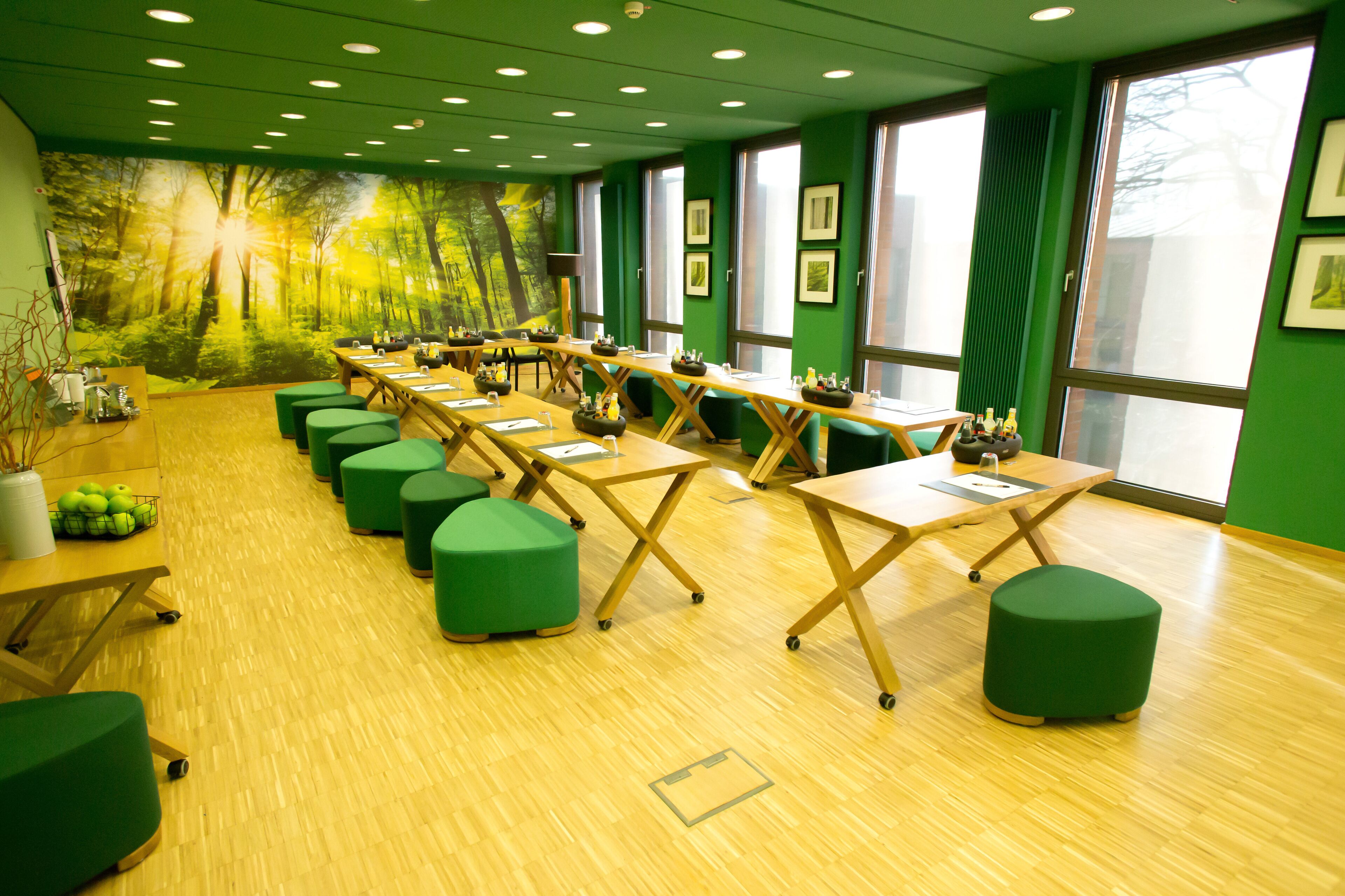 A conference room with green walls, large windows, and a forest mural.