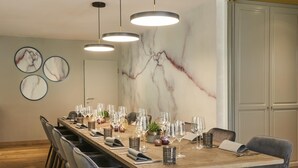 A dining area with a marble wall, a long wooden table set for a meal, and modern pendant lighting. - QUARTIER 82 by Arcadeon (Hagen)