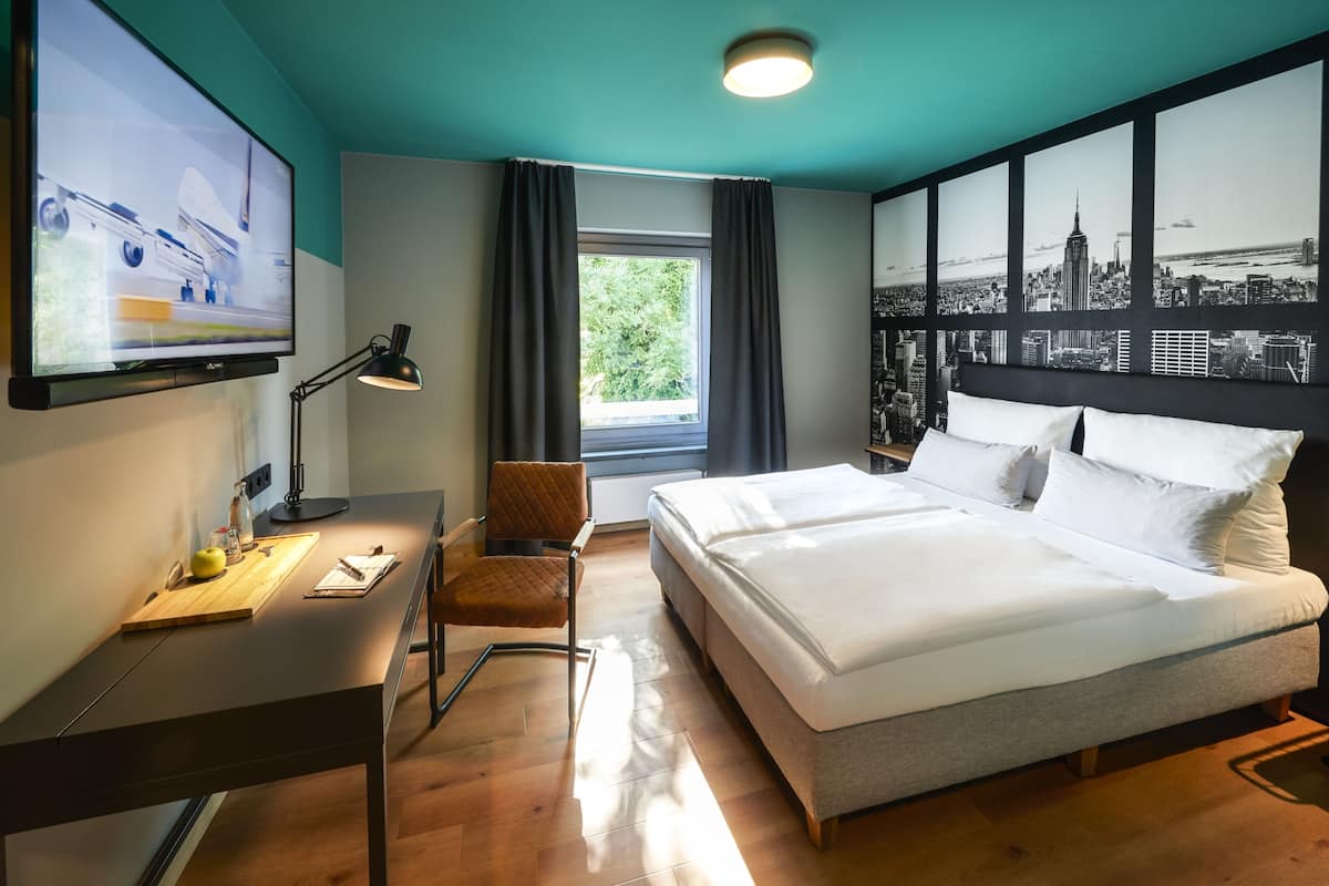 Une chambre d’hôtel moderne avec un grand lit, un bureau équipé d’un ordinateur, une chaise et un téléviseur fixé au mur.