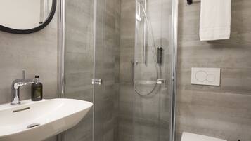 Un baño moderno con ducha de vidrio, lavamanos blanco y retrete.
