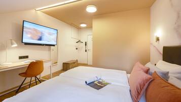 A modern hotel room with a large bed, a desk with a chair, a television, and a bathroom door.
