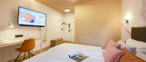 Una habitación de hotel moderna con una cama grande, un escritorio con silla, un televisor y la puerta del baño.