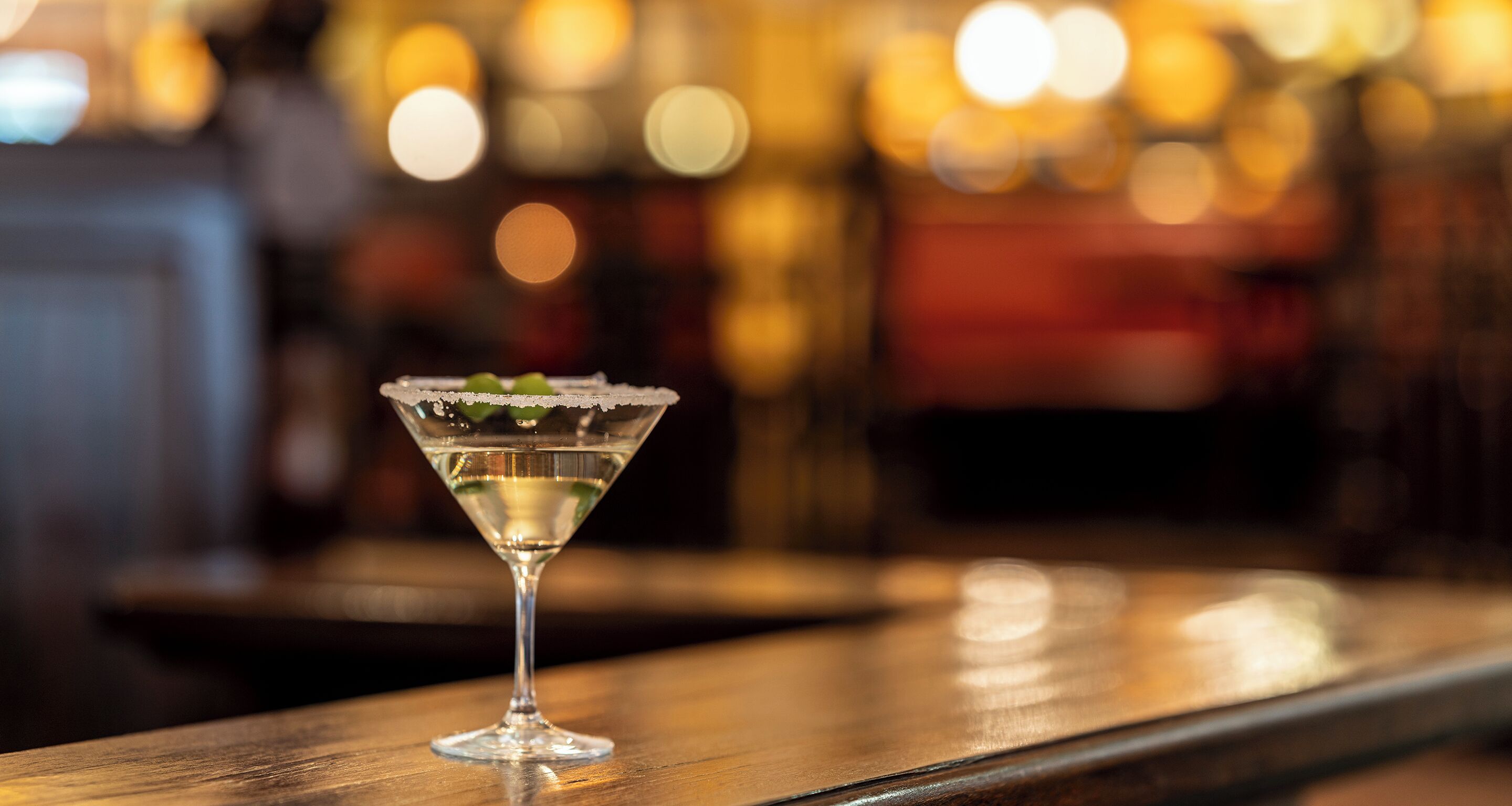 A martini glass with a garnish on a wooden bar counter.