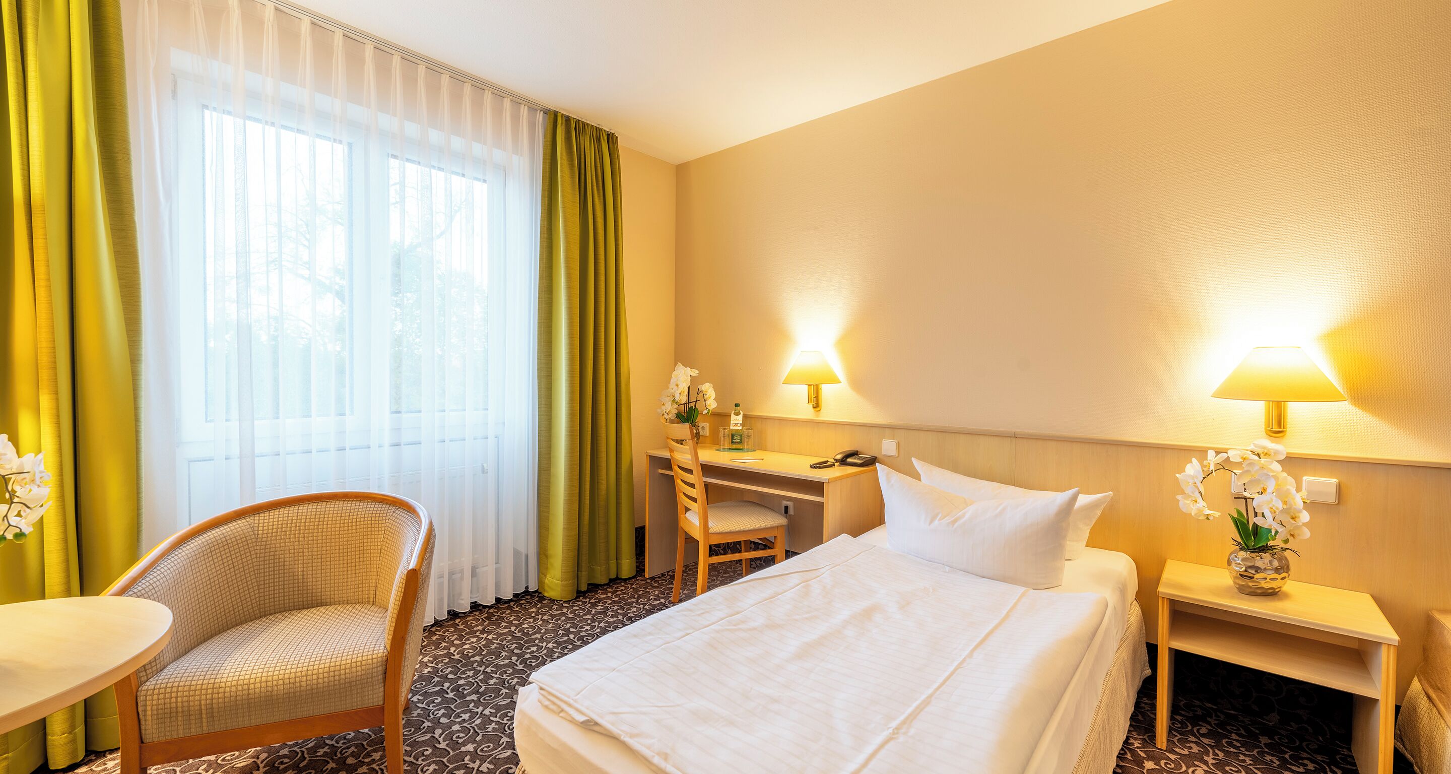 A hotel room with a bed, a desk, a chair, and a small table.