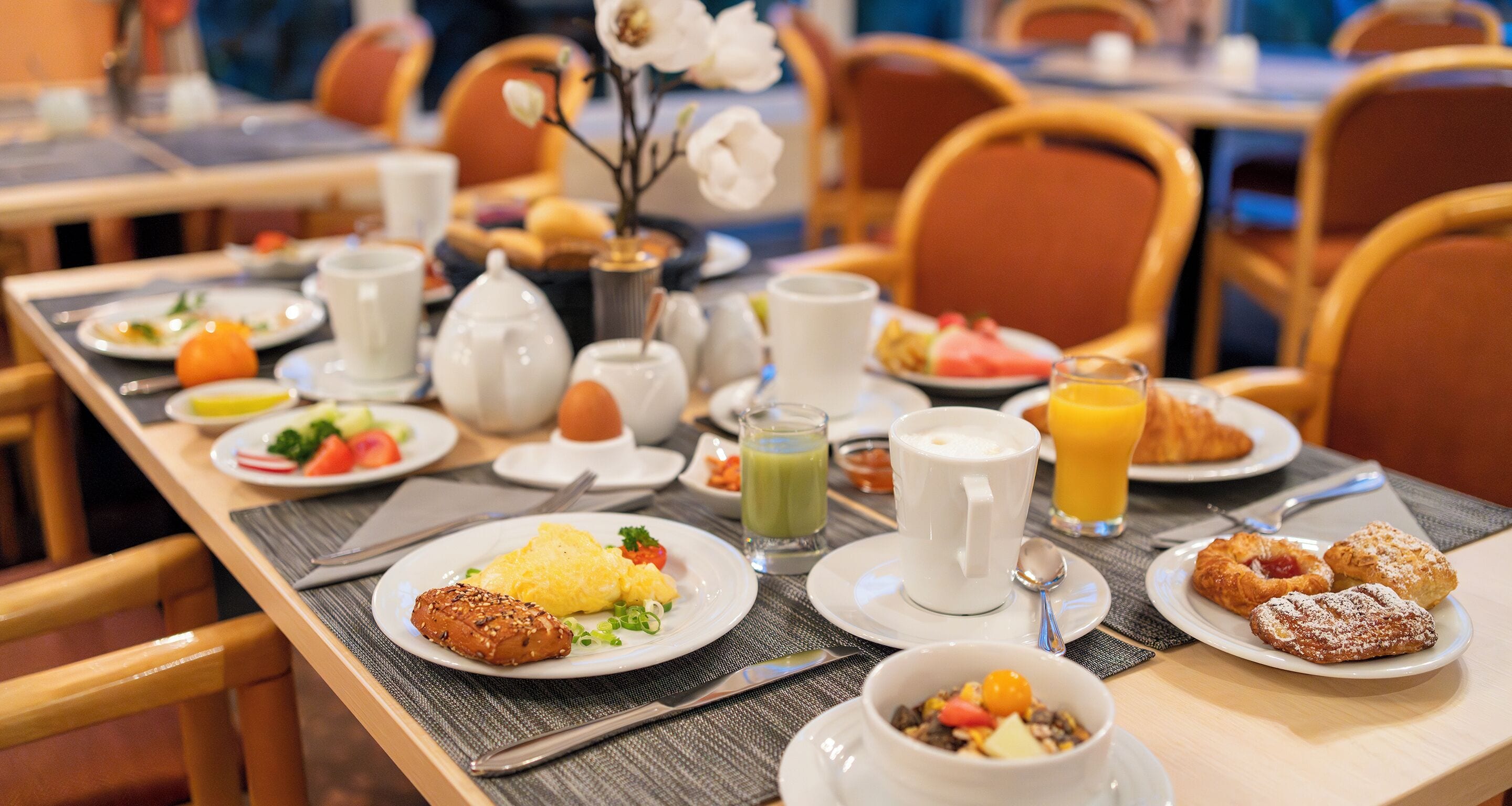 A breakfast setting with plates of food, a coffee pot, and a juice glass.