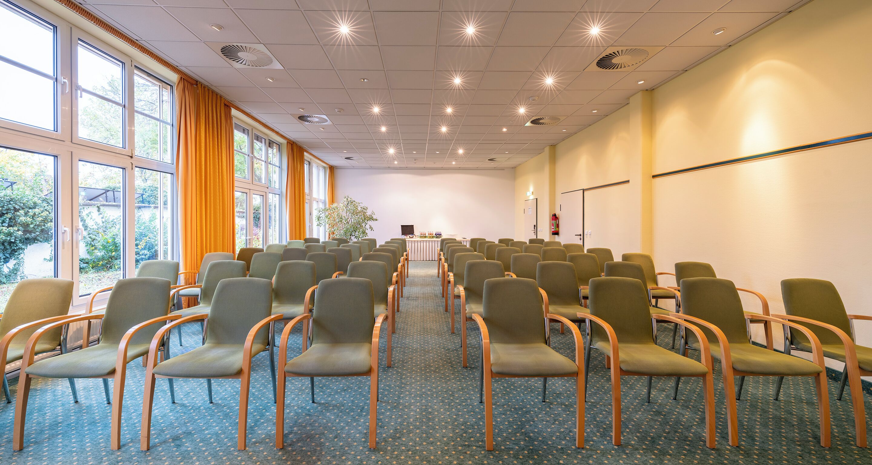 A conference room with rows of chairs, large windows, and a carpeted floor.