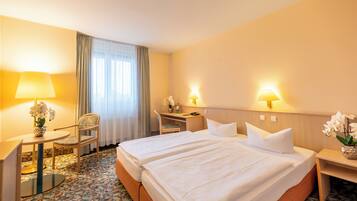 A hotel room with two beds, a desk, a chair, a lamp, and a vase with flowers.