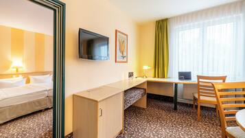 A hotel room with a bed, desk, chair, TV, and a window with curtains.