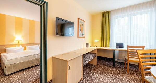 Habitación de hotel con cama, escritorio, silla, televisión y ventana con cortinas.