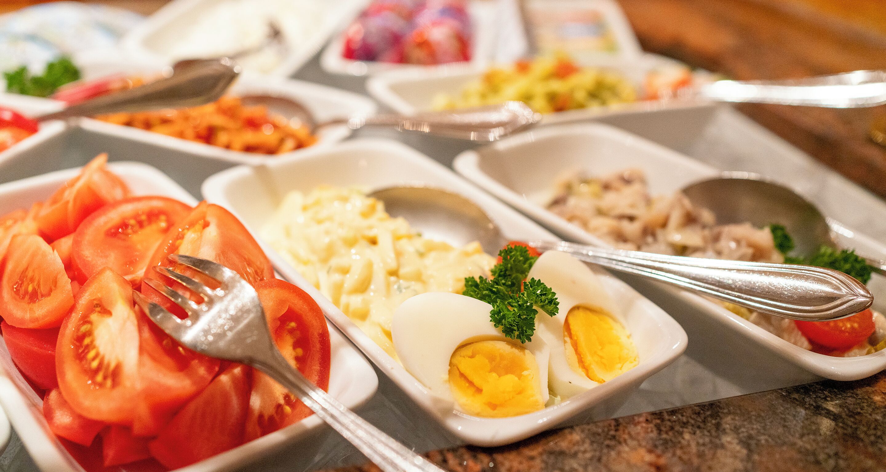 Un bufé con diversos platos, incluyendo tomates en rodajas, huevos y una ensalada.