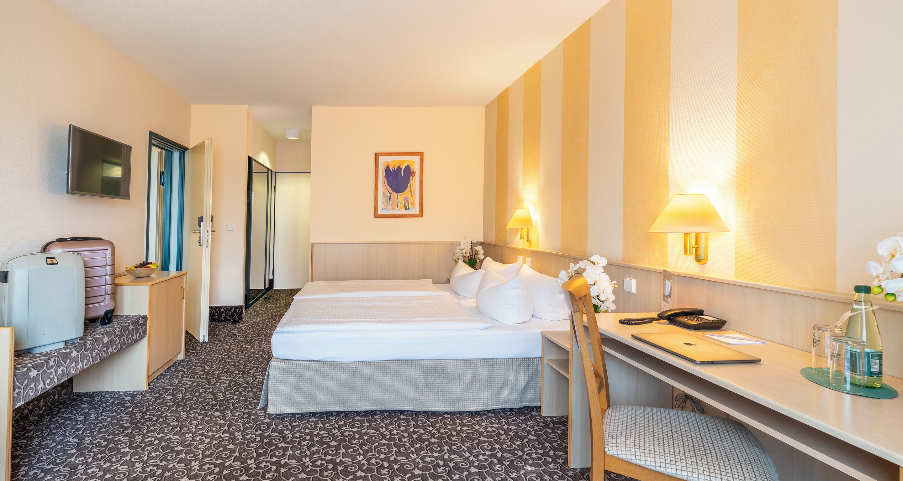 Ett hotellrum med två sängar, ett skrivbord, en stol, en TV och en dörr till badrummet.
