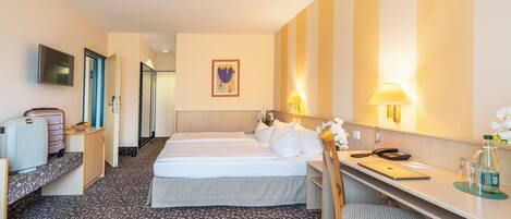 Habitación de hotel con dos camas, un escritorio, una silla, un televisor y la puerta del baño.