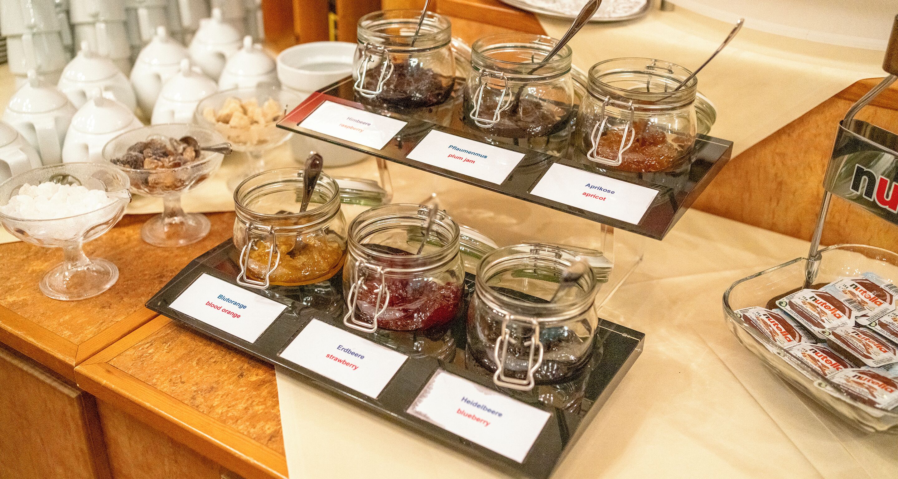 A buffet with various jams and spreads, including strawberry, plum, apricot, and blueberry.