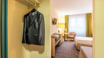 Une chambre d’hôtel avec un lit, un bureau, une chaise, une lampe et un manteau accroché au mur.