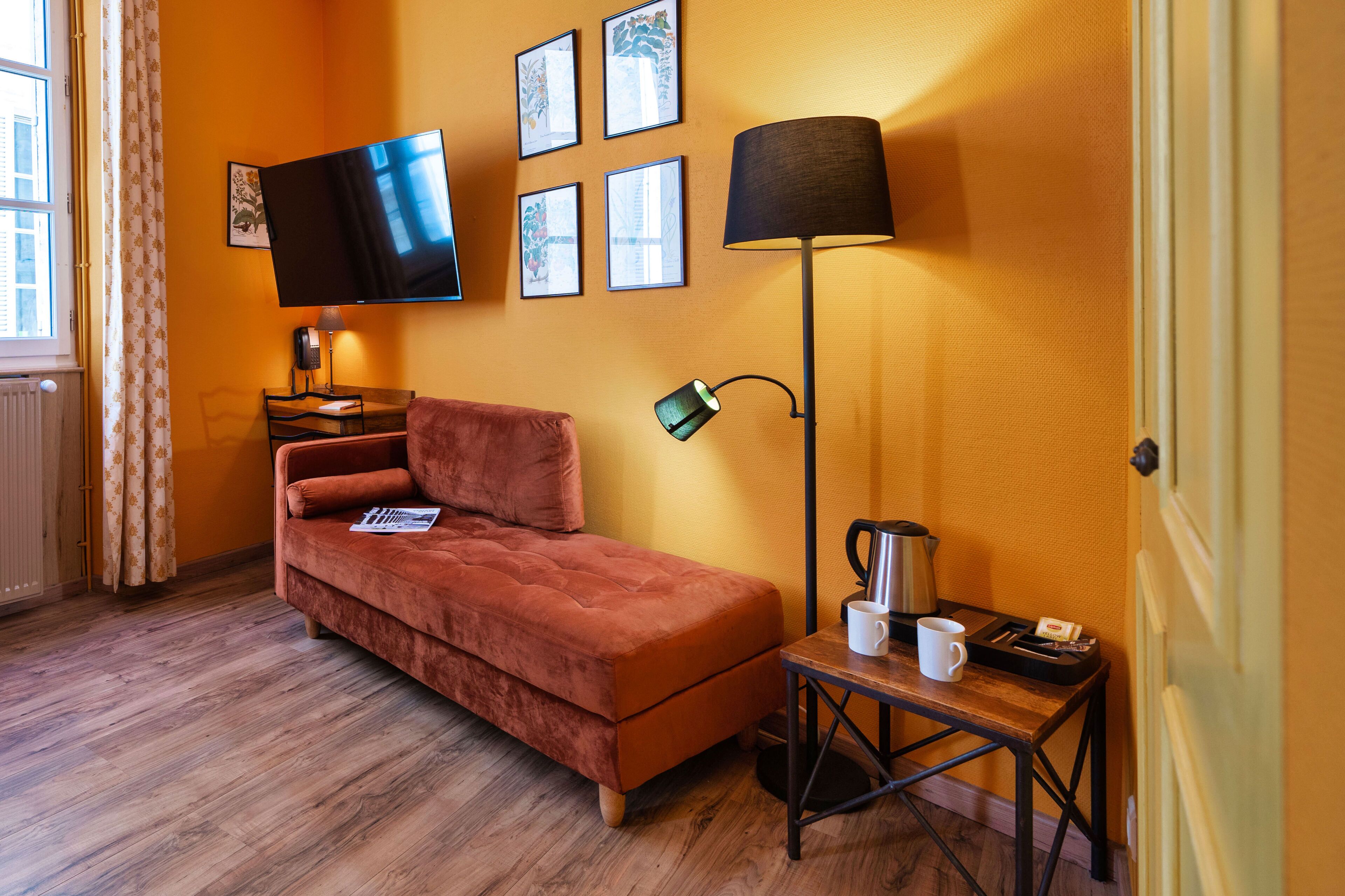 Una habitación con sofá, televisor de pantalla plana, lámpara y una mesita con cafetera y tazas.