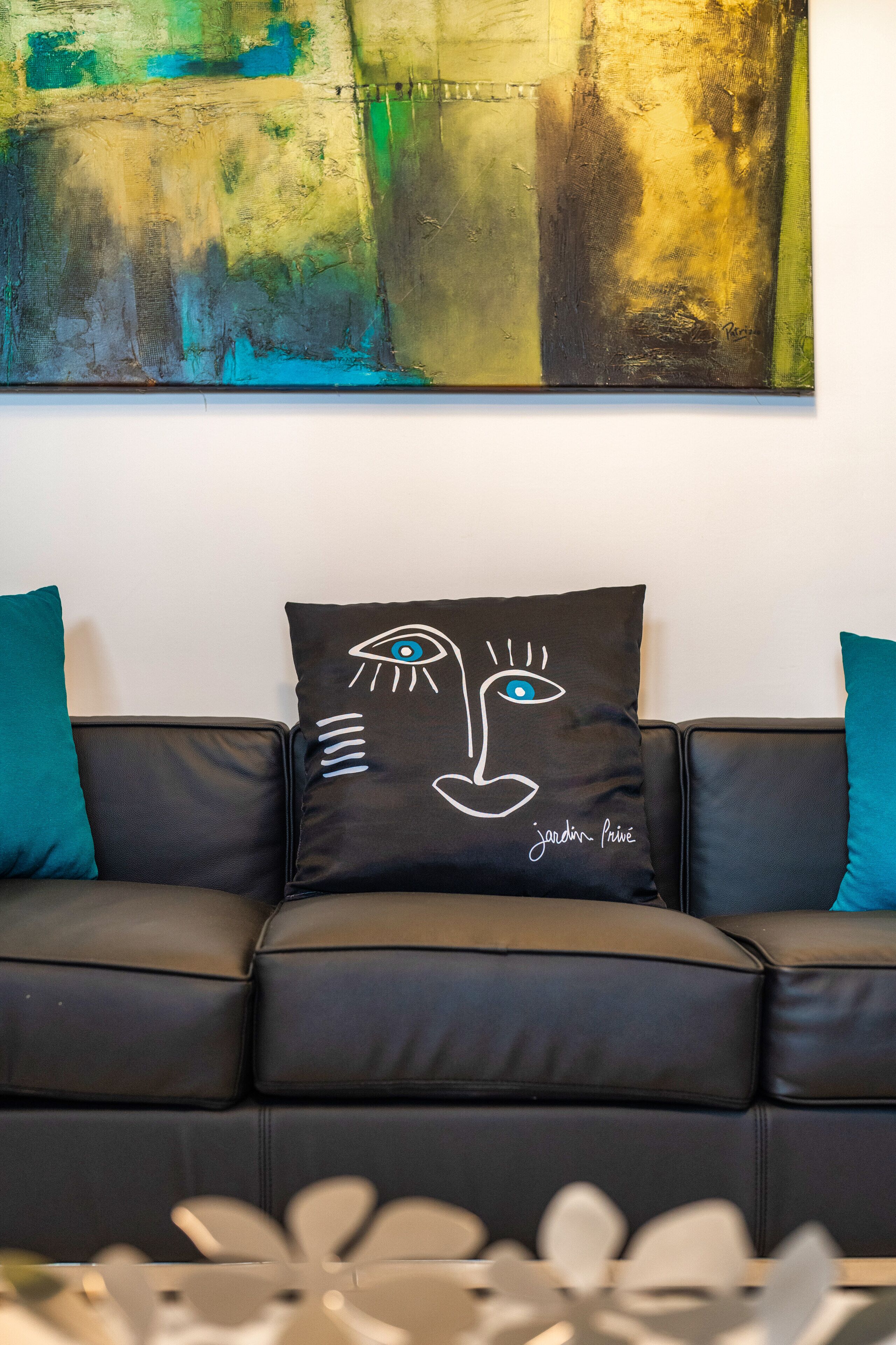 A black leather sofa with teal cushions and a wall-mounted abstract painting.