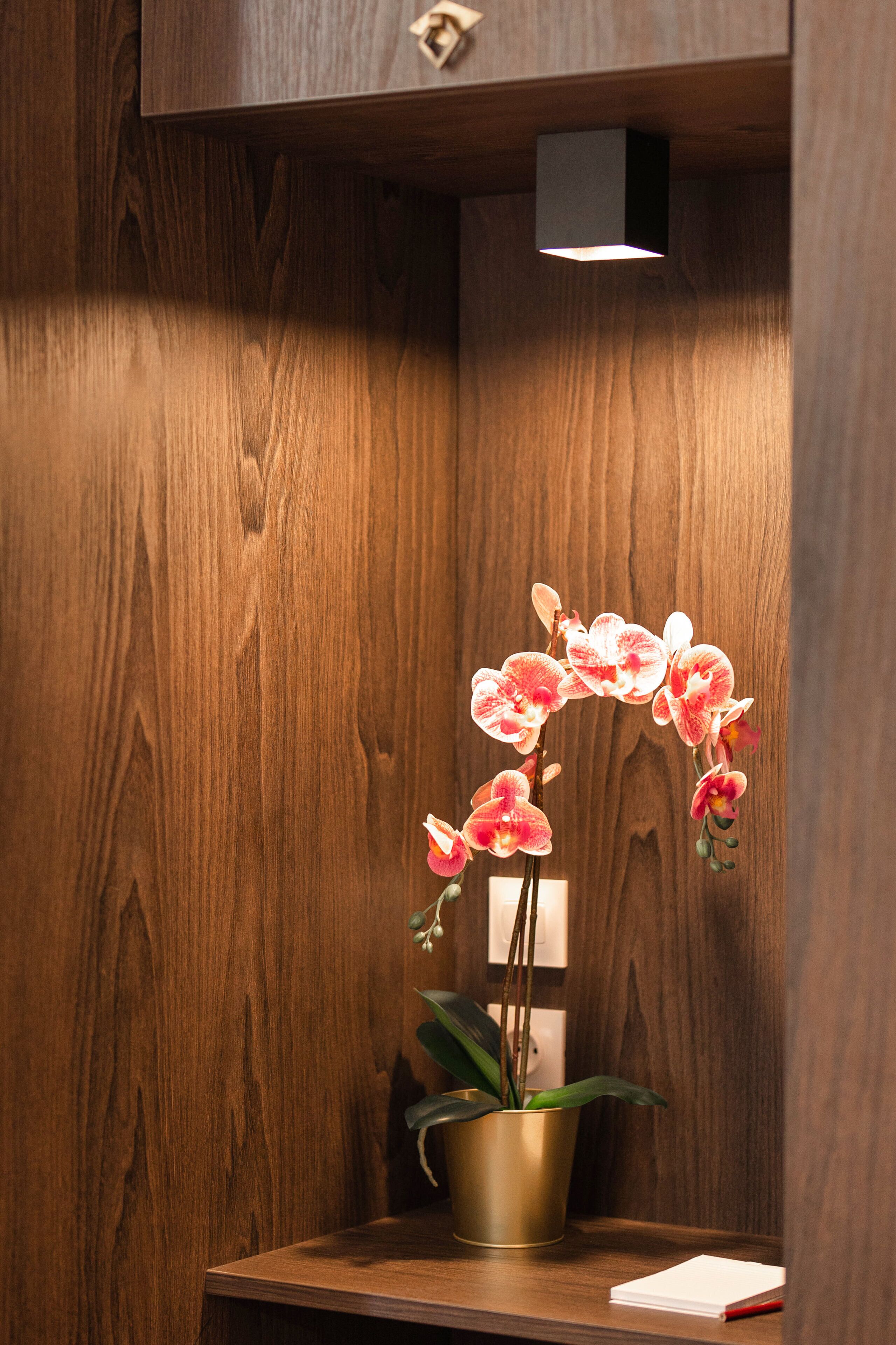 Un mueble de madera con un pequeño escritorio, una orquídea en maceta y un bloc de notas.