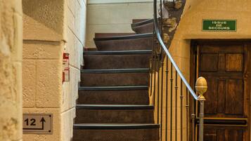 A staircase with a handrail, a sign indicating the direction to the issue de secours, and a wooden door at the bottom.