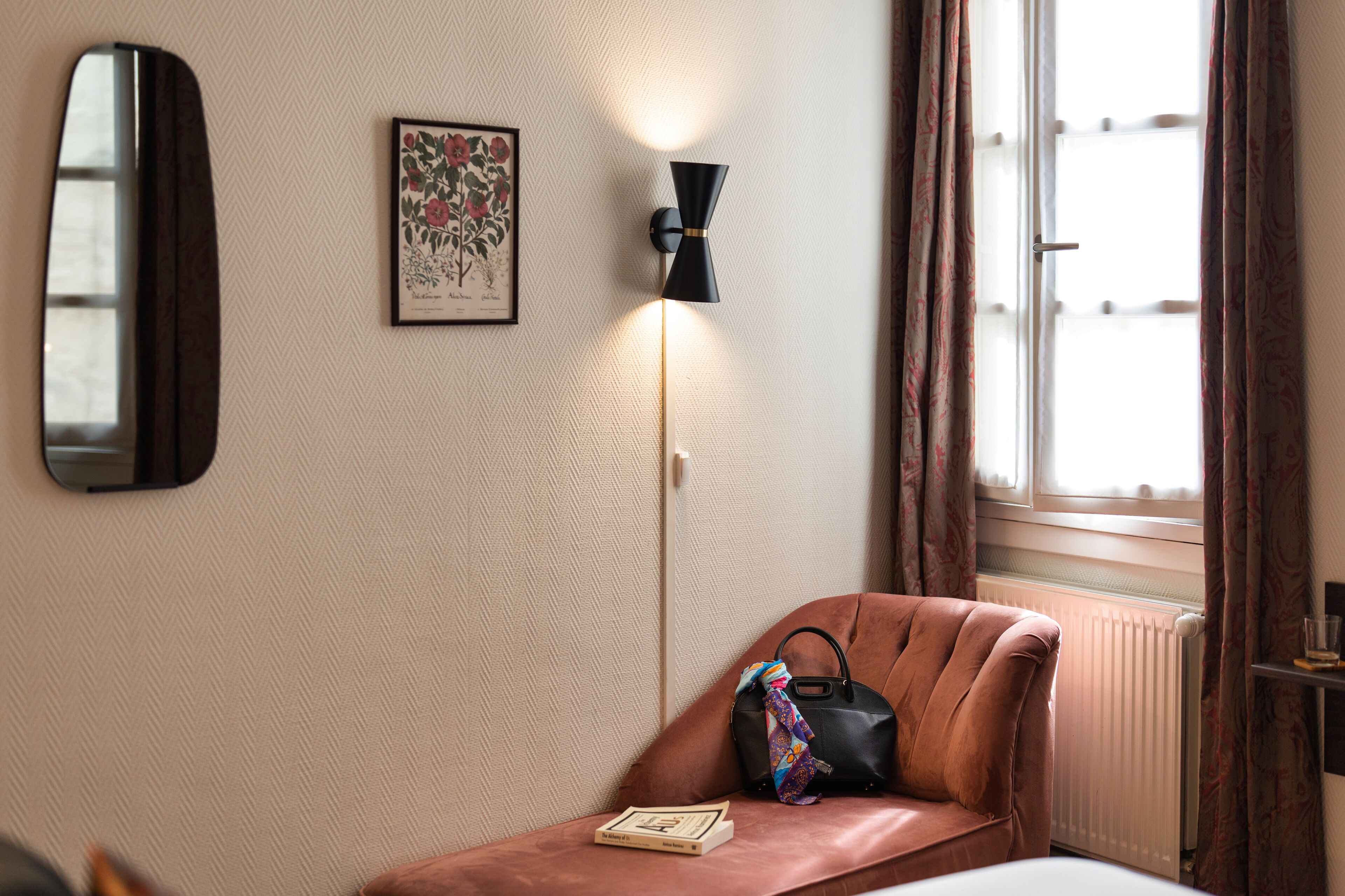 A hotel room with a brown leather armchair, a black floor lamp, a framed botanical print, and a window with curtains.