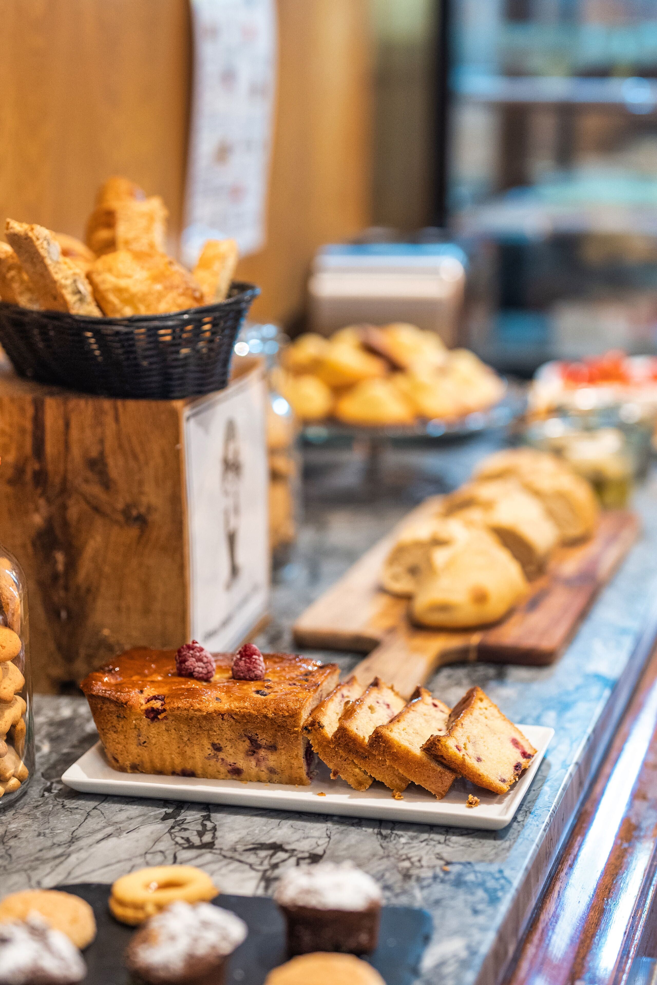 A variety of baked goods displayed on a marble countertop, including bread, pastries, and a cake with raspberry garnish.