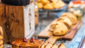 A variety of baked goods displayed on a marble countertop, including bread, pastries, and a cake with raspberry garnish.