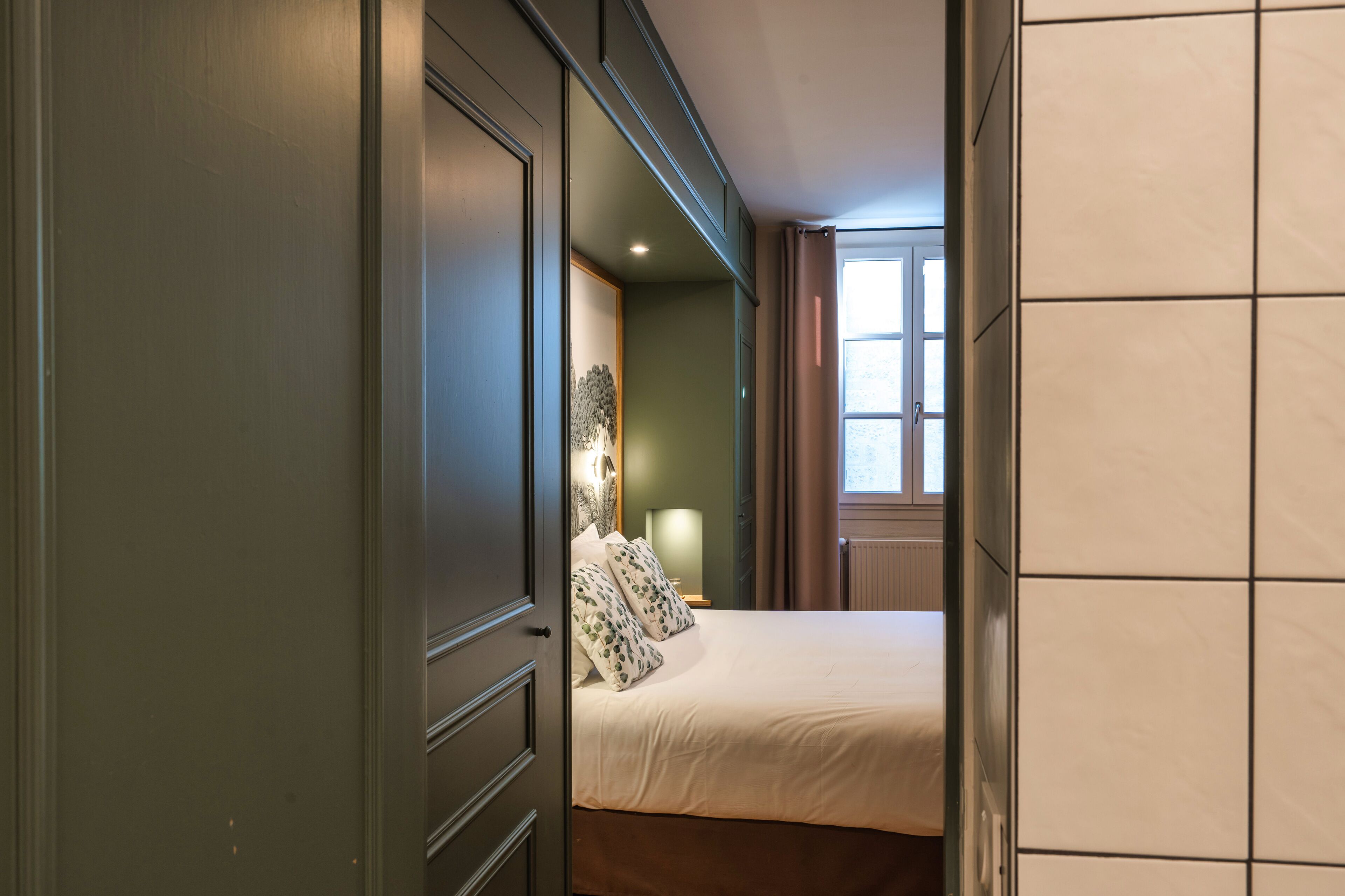 Un dormitorio con cama, mesita de noche, lámpara y ventana con cortinas.
