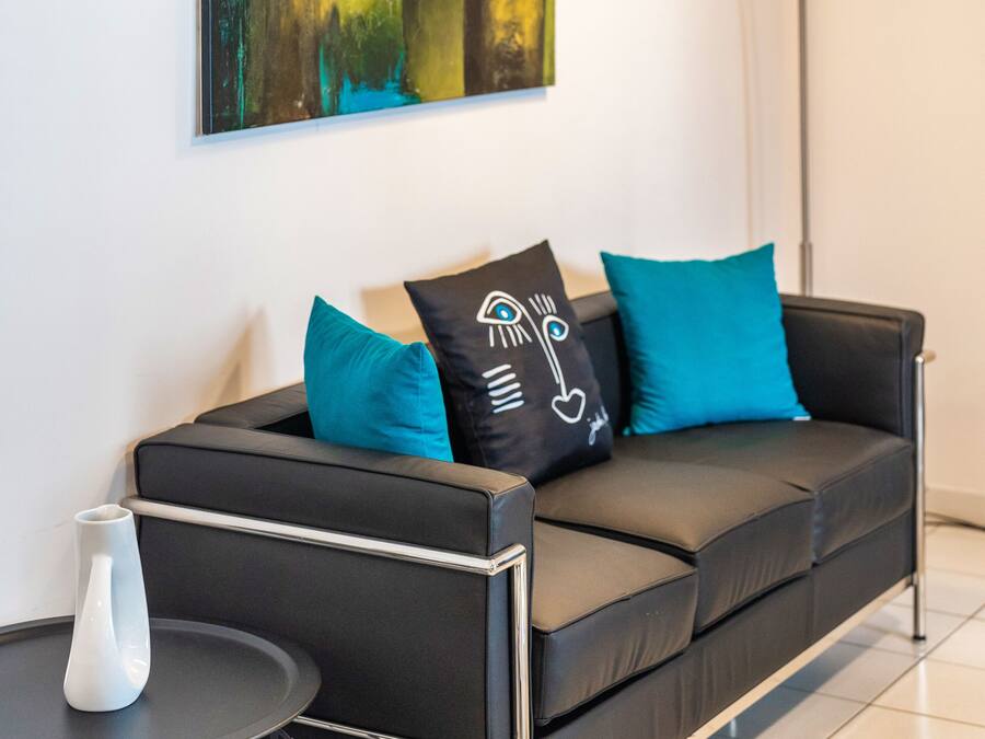 A modern living room with a black sofa, teal cushions, a white vase, and a floor lamp.