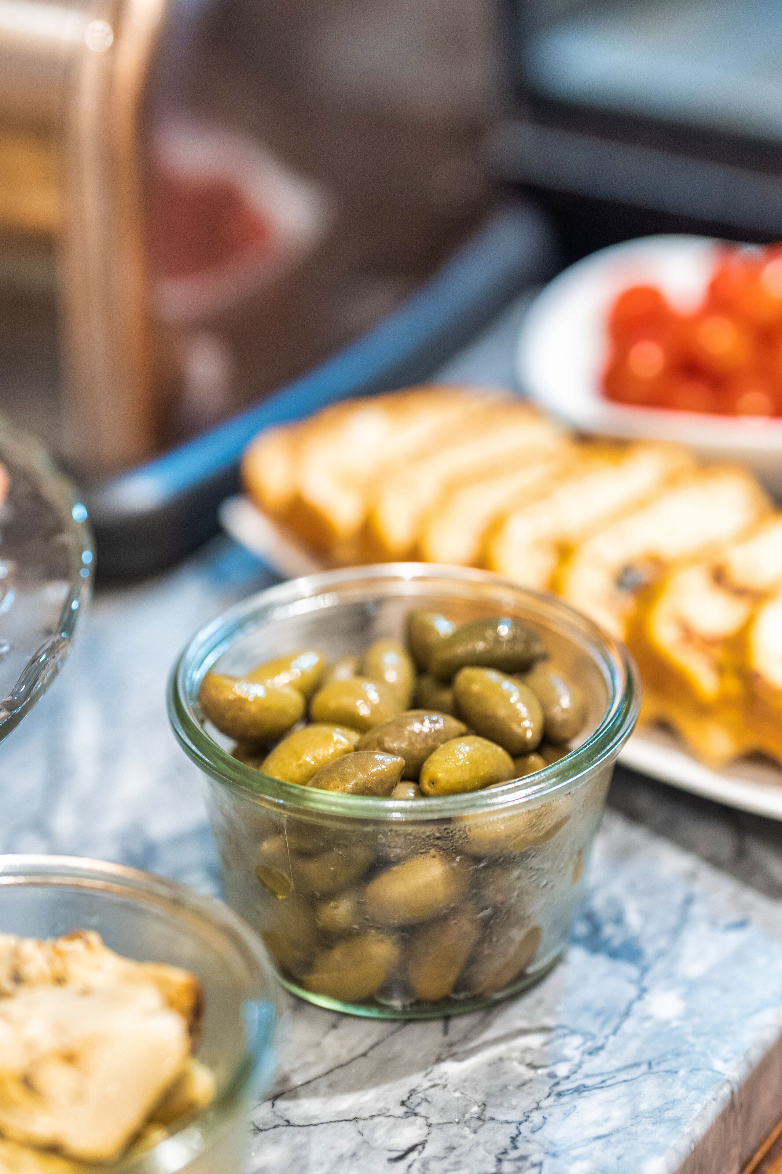 A glass jar filled with olives on a marble countertop.
