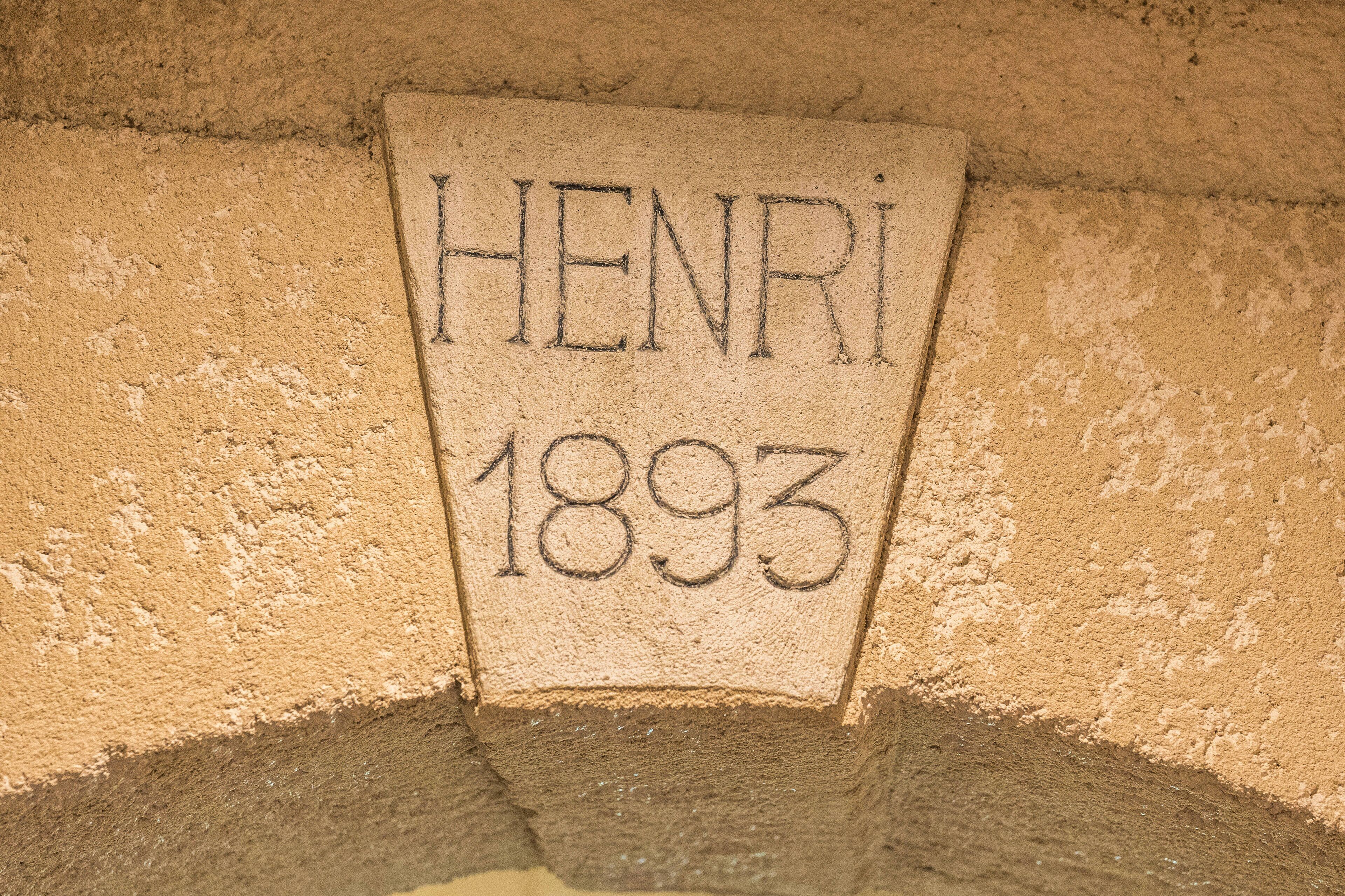 Een stenen plaquette met de naam 'HENRI' en het jaar '1893' in gegraveerd.