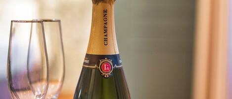 Una botella de champán George La Côme Premier Cru Brut, dos copas de vino vacías y un plato con pasteles sobre una mesa.