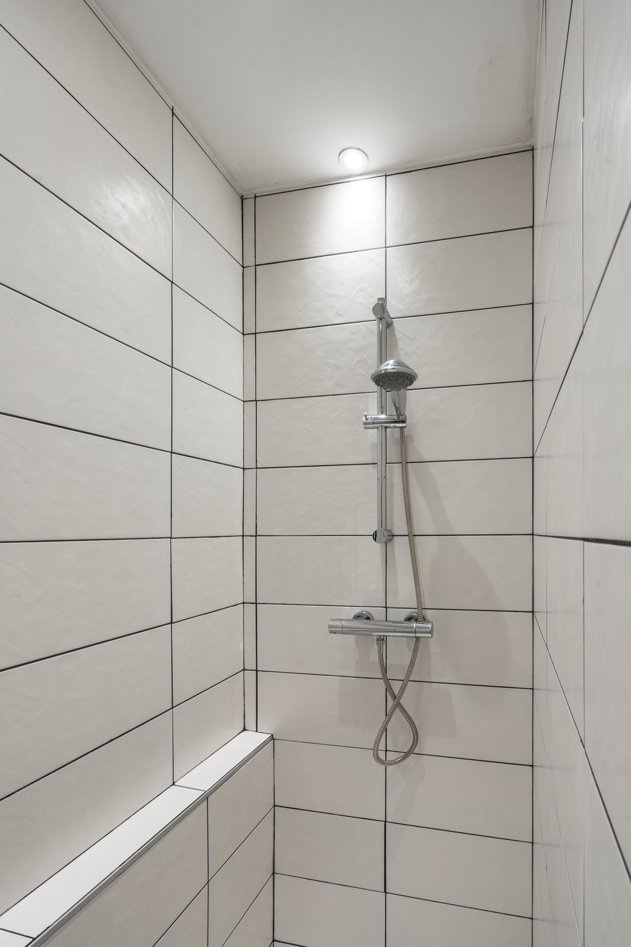 Une douche équipée d’un pommeau de douche à main et d’un robinet mural dans une salle de bain carrelée.