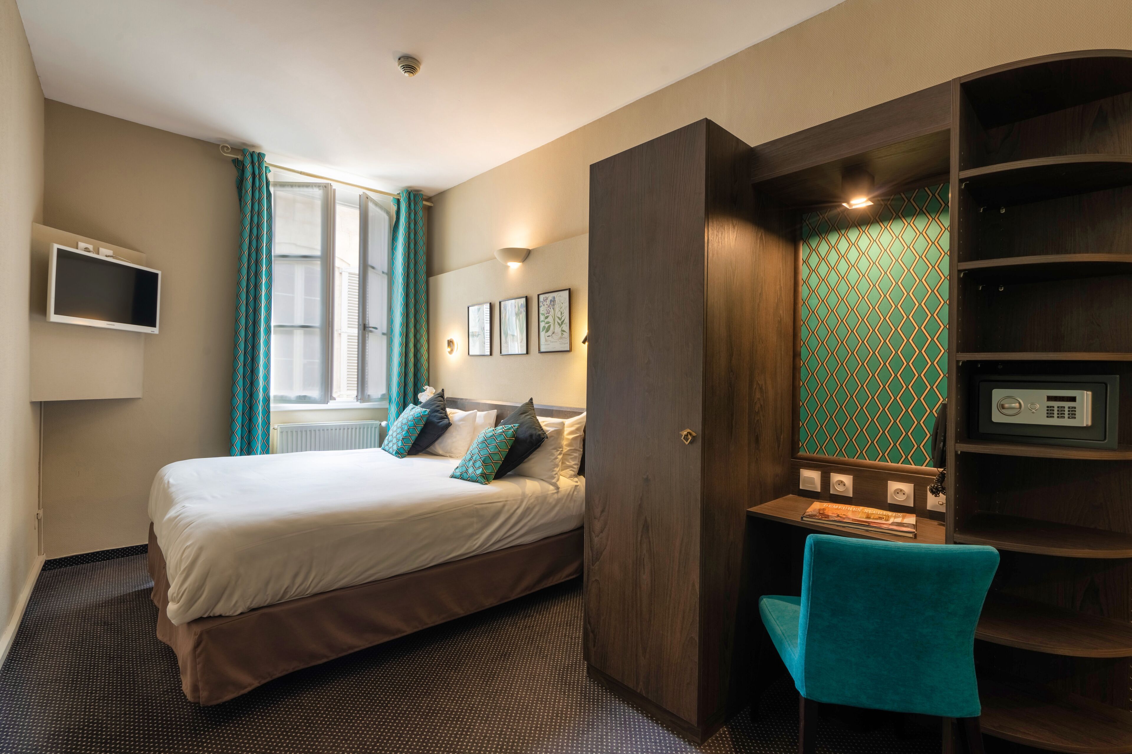 Habitación de hotel con cama, escritorio, silla, televisor y ventana con cortinas.