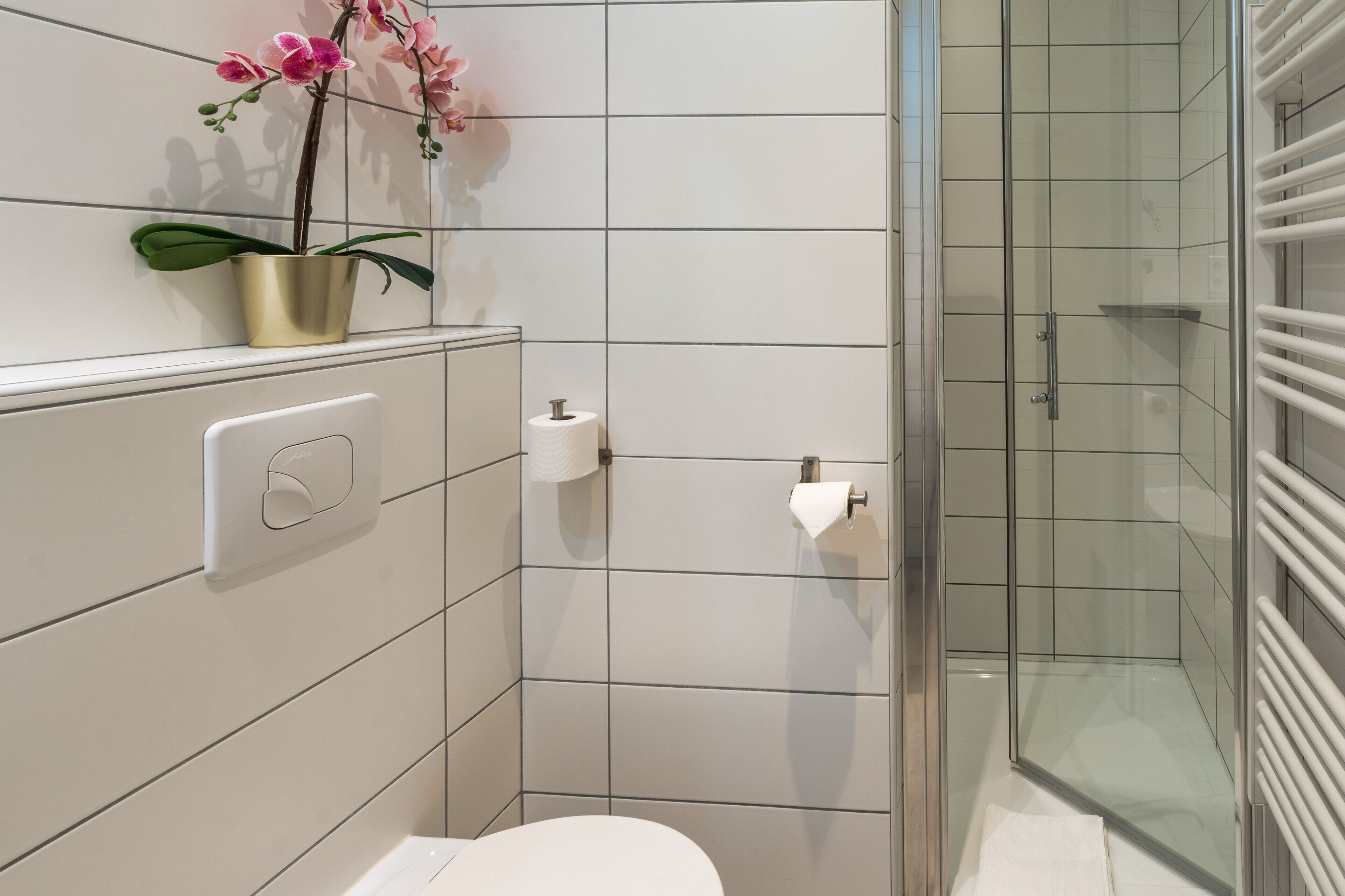 Une salle de bain moderne avec des toilettes, une douche en verre et une orchidée en pot.