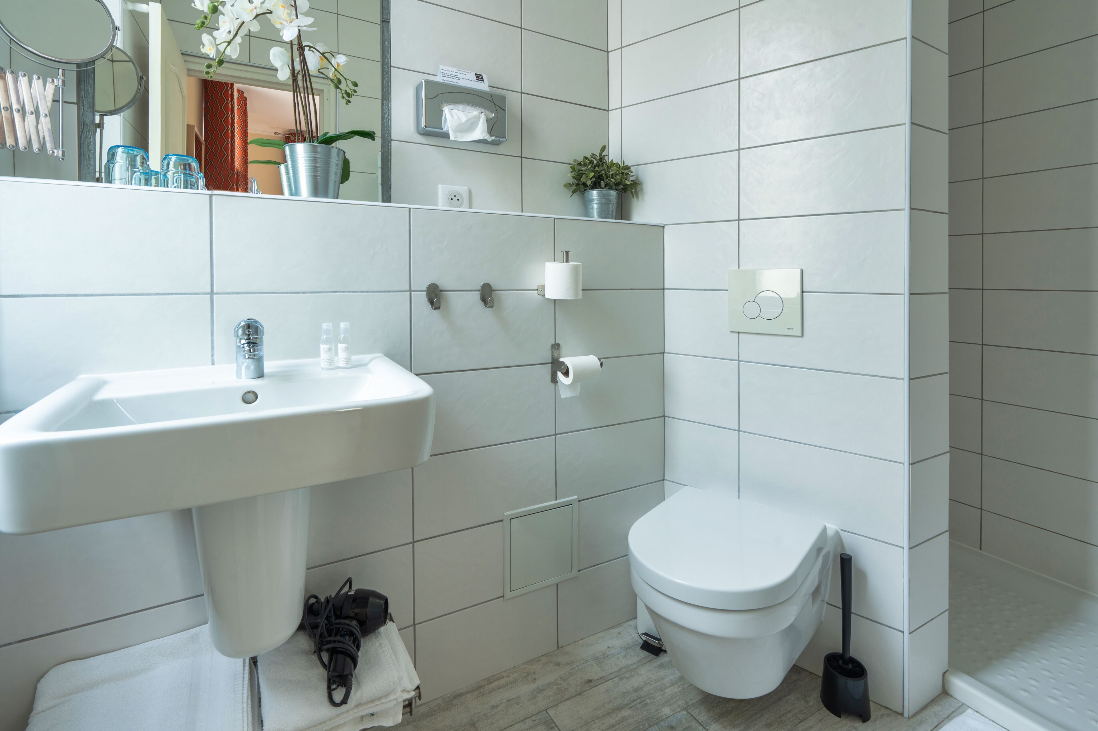A modern bathroom with a white sink, toilet, and a small potted plant on the wall.