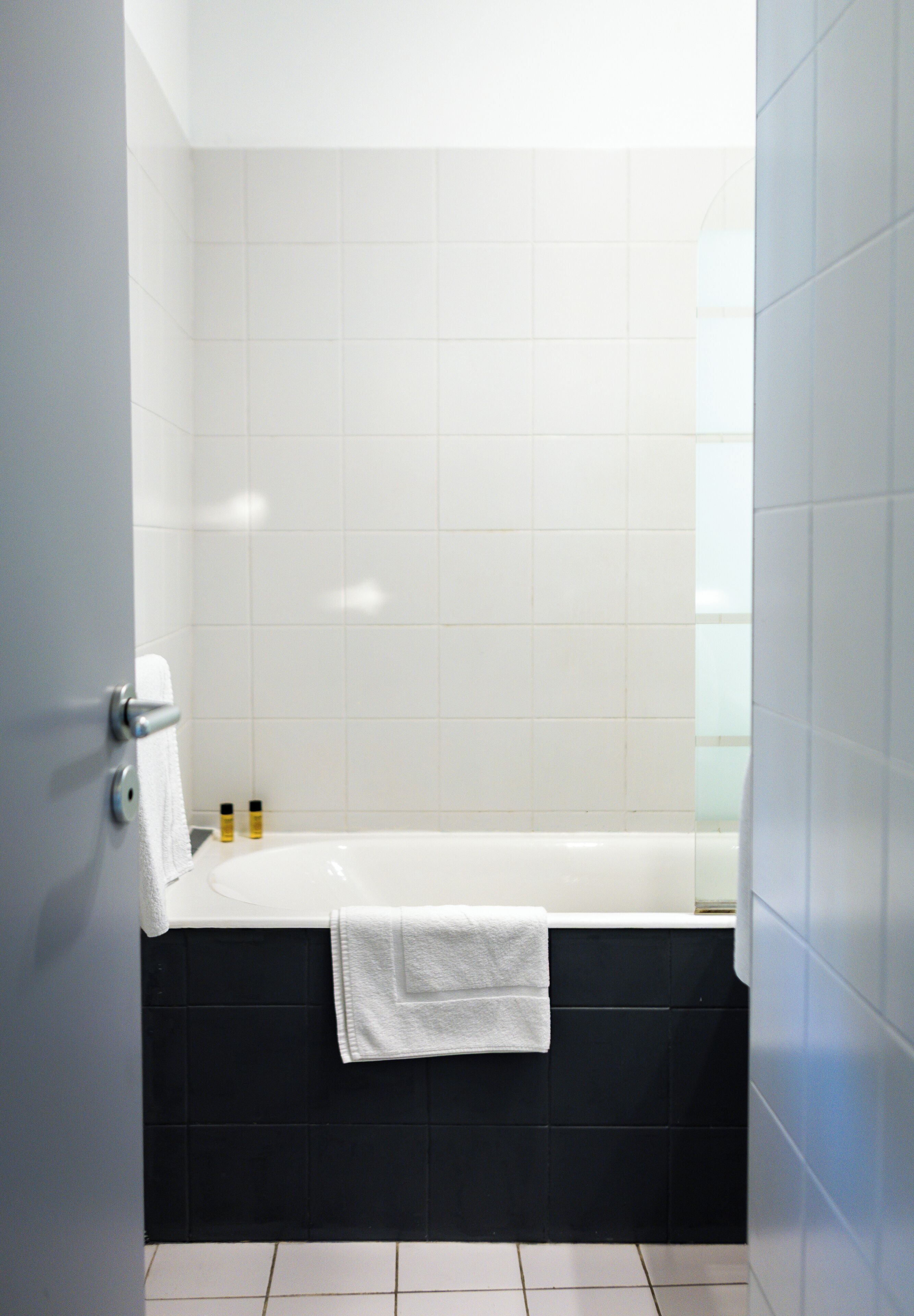 A bathroom with a white bathtub, black tiled walls, and a white towel on the tub.