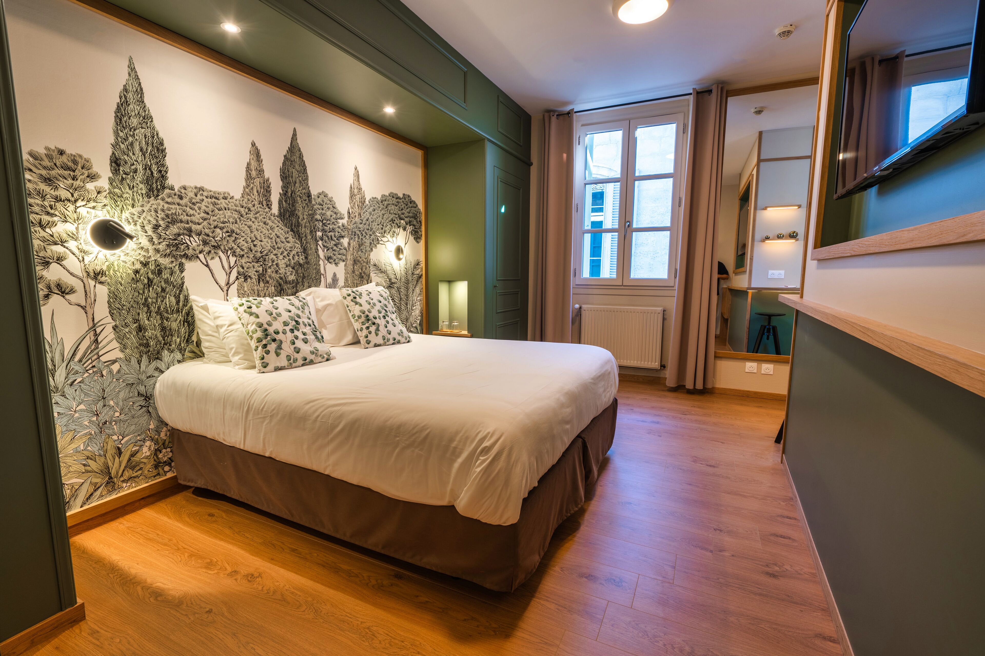 Une chambre avec un grand lit, une fresque murale, une fenêtre avec des rideaux et un téléviseur fixé au mur.
