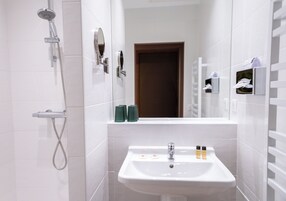 A modern bathroom with a white sink, a handheld showerhead, and a mirror with a wooden door in the background.