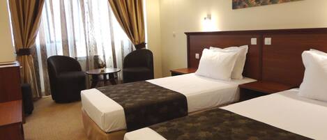 A hotel room with two beds, a desk, a chair, and a small table.