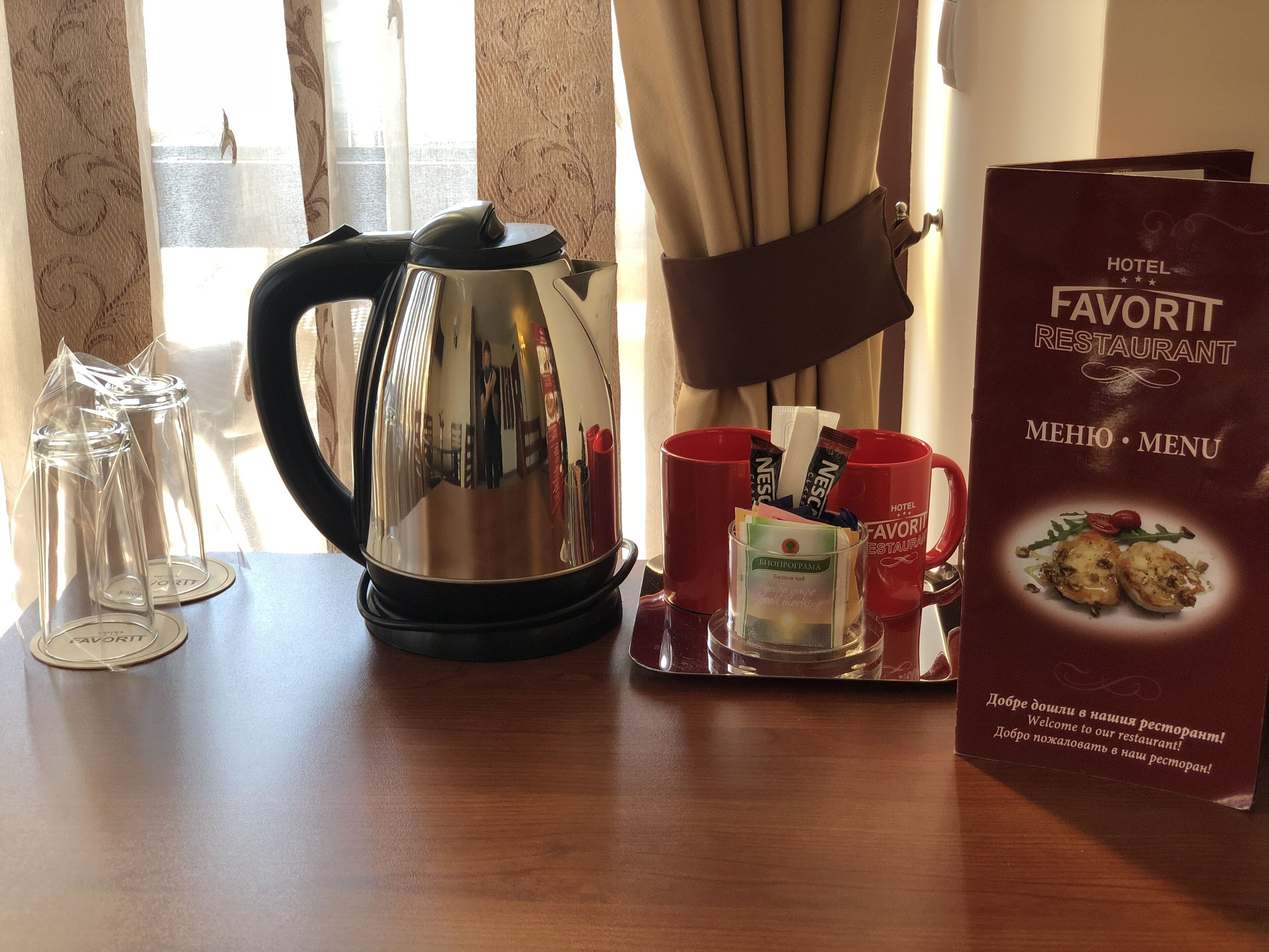 A hotel room with a table set for breakfast, including a kettle, glasses, and a menu.