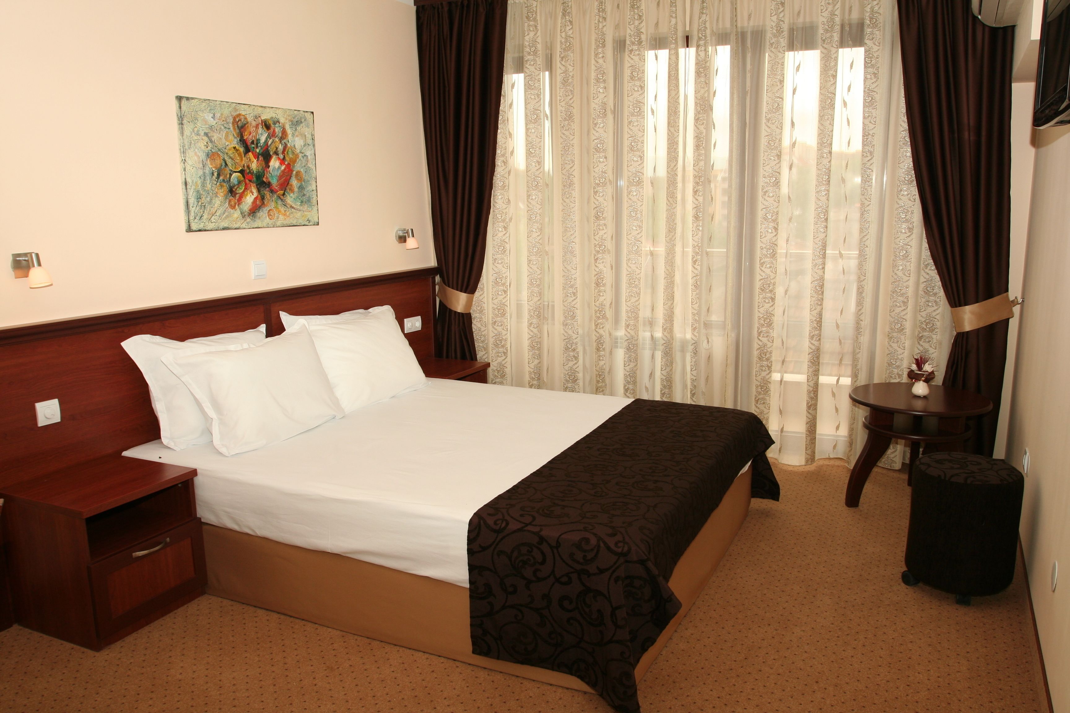 A neatly made bed with white linens, a wooden headboard, a bedside table with a lamp, and a painting on the wall.
