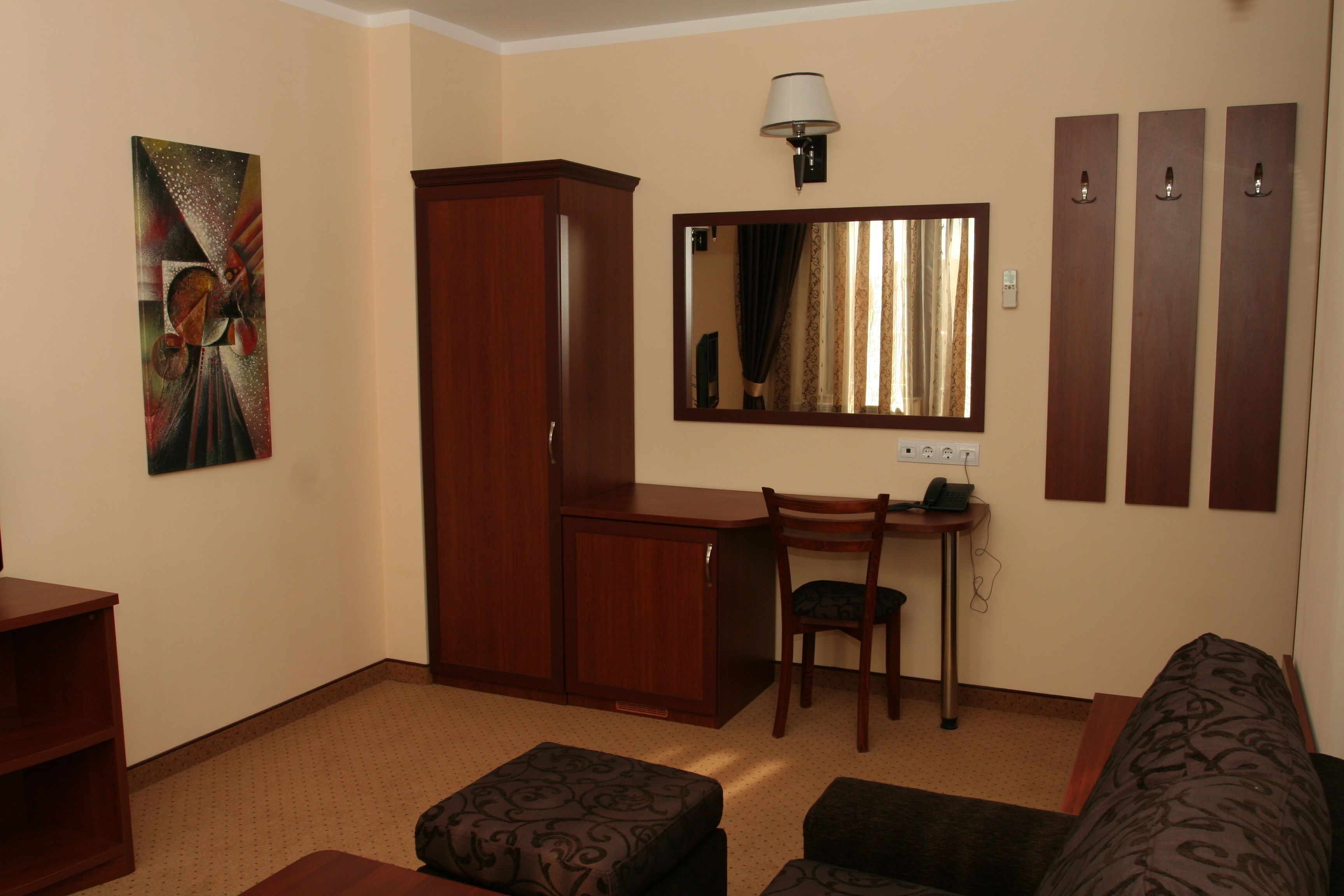 Habitación de hotel pequeña con cama, escritorio, silla, armario, un cuadro, espejo y lámpara.