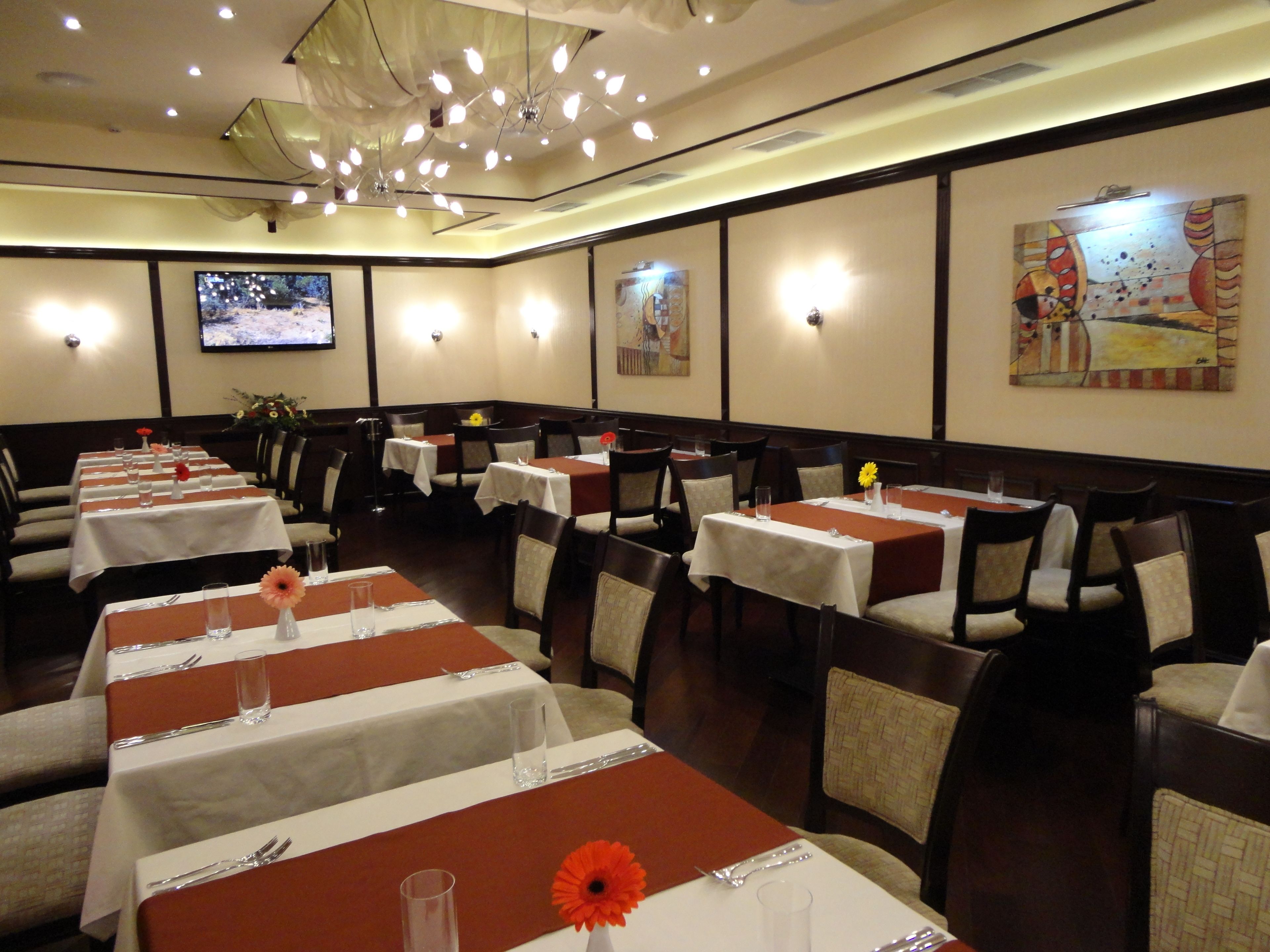 Een restaurant met meerdere tafels, elk voorzien van bestek en glazen, en een televisie aan de muur.